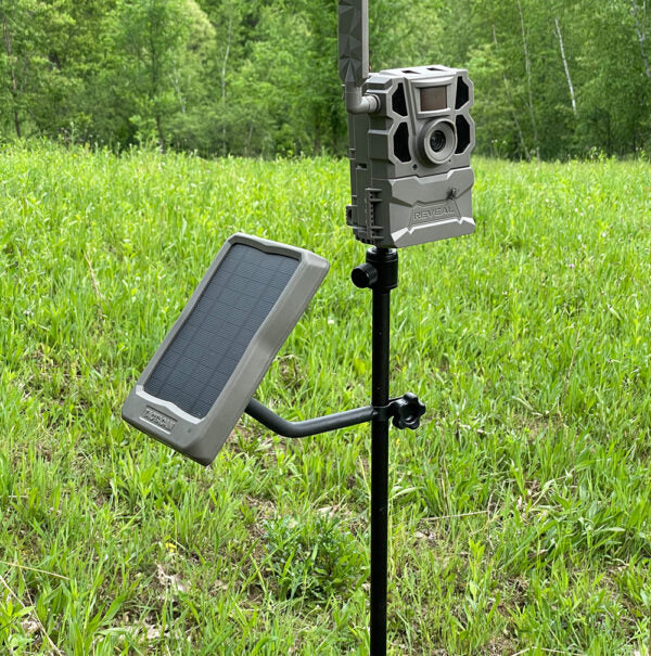 Hunter setting up hunting camera accessories in a wooded field.